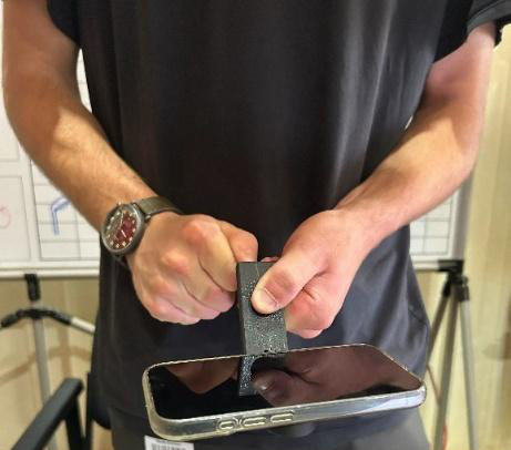 Hands holding a black 3D-printed finger that is lifting a smartphone by its edge